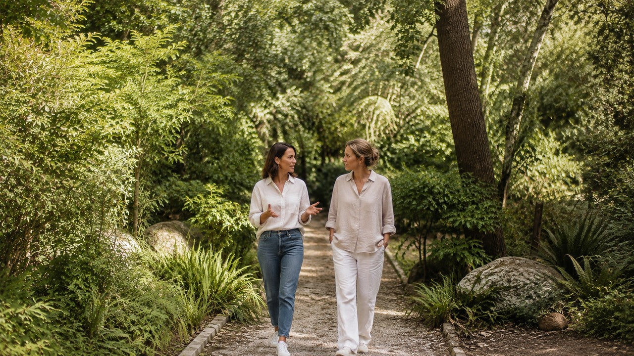 Two women walking and talking in a softly sunlit botanical woodland garden