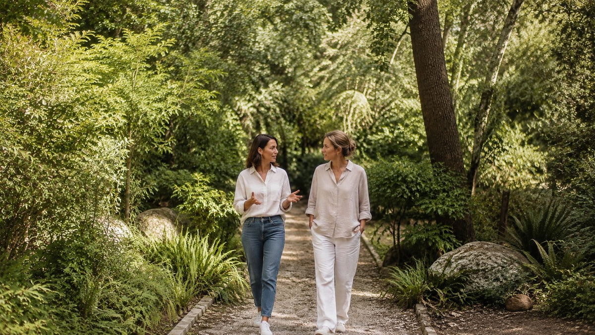 Two women walking and talking in a softly sunlit botanical woodland garden